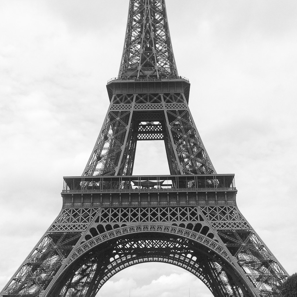 Mid section of the Eiffel Tower in black and white with the cloud covered sky in the backround