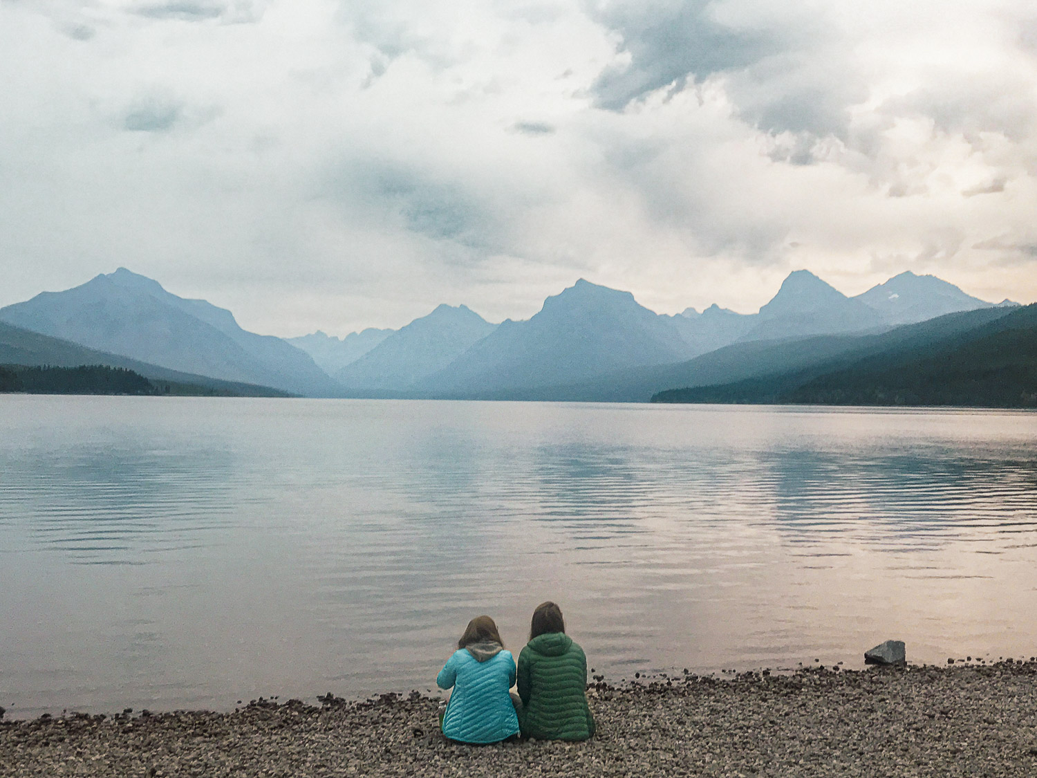 Two people sitting on the edge of McDonald lake watching the sun rise in Glacier Naitonal Park