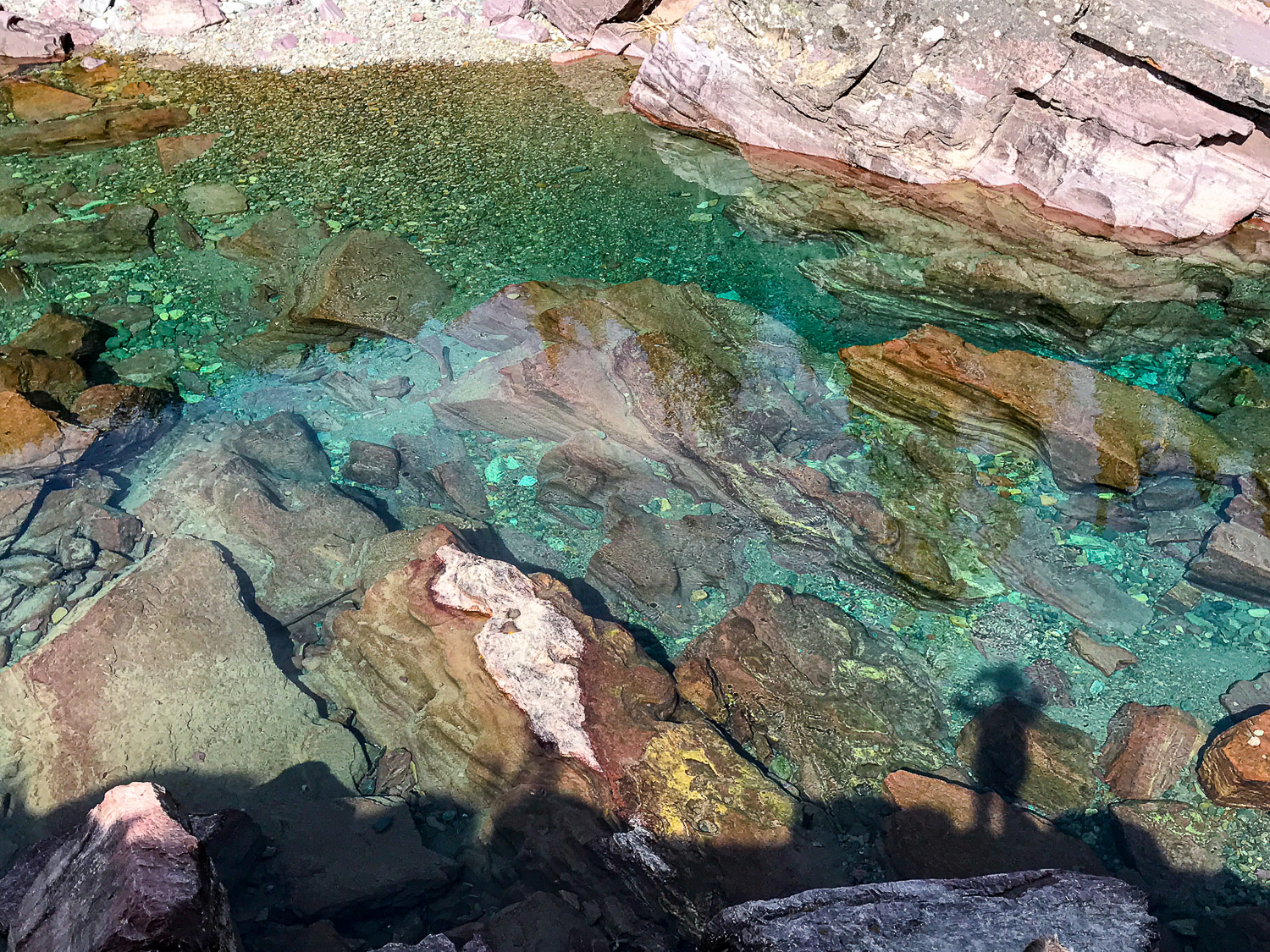 Red rocks visible below crystal clear blue green waters in Glacier National Park