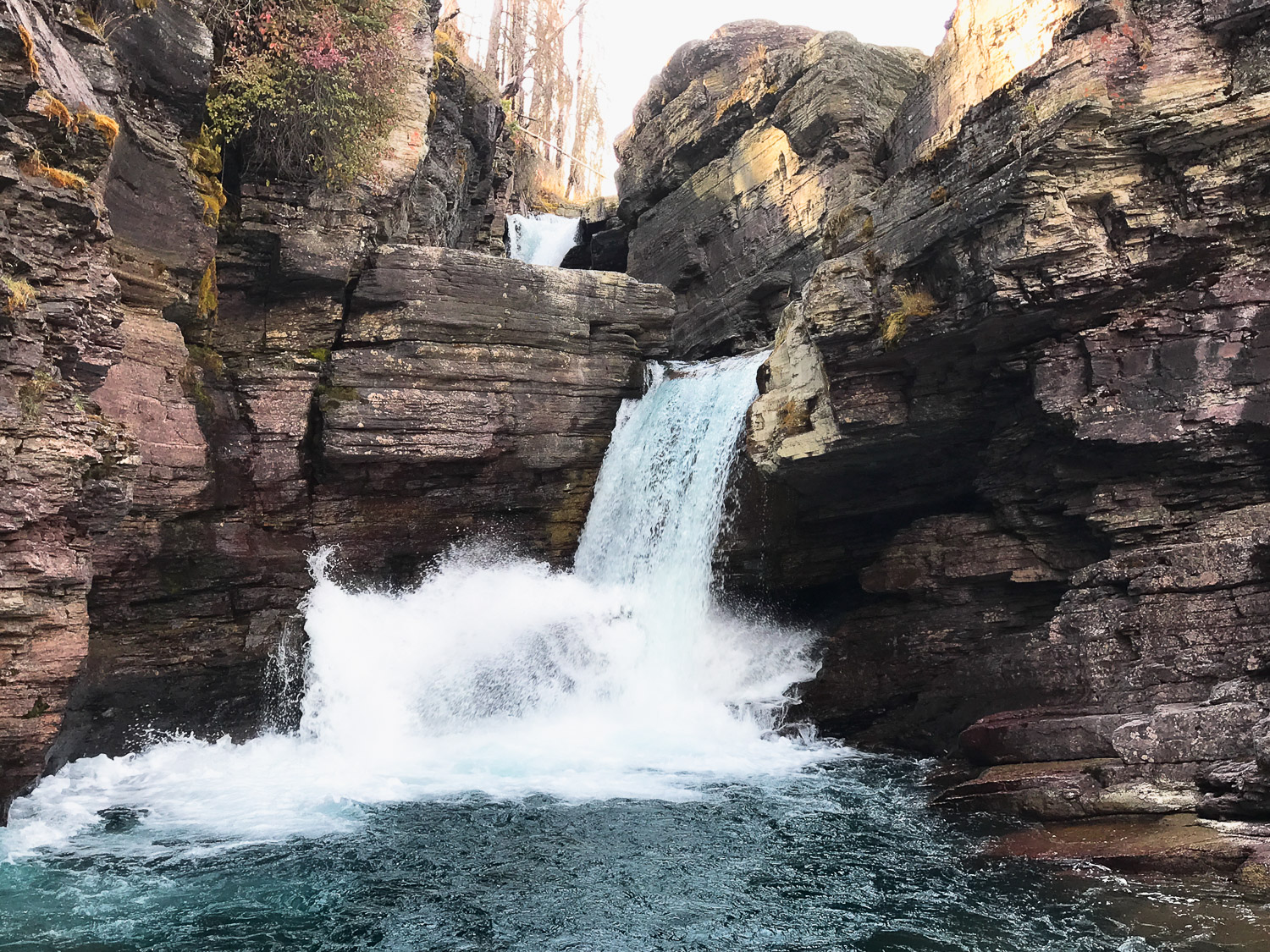 Two cascading falls flowing down layered rock walls in Glacier National Park