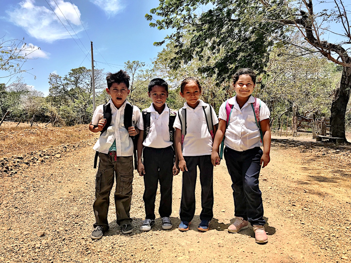 Four Nicaraguan school children wearing school uniforms of white tops and dark jeans posing for the photo