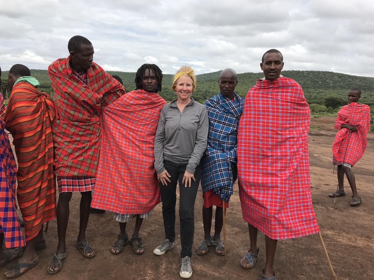 Four Maasai wearing traditional colorful red and blue shukas stand next to a woman posing for the photo