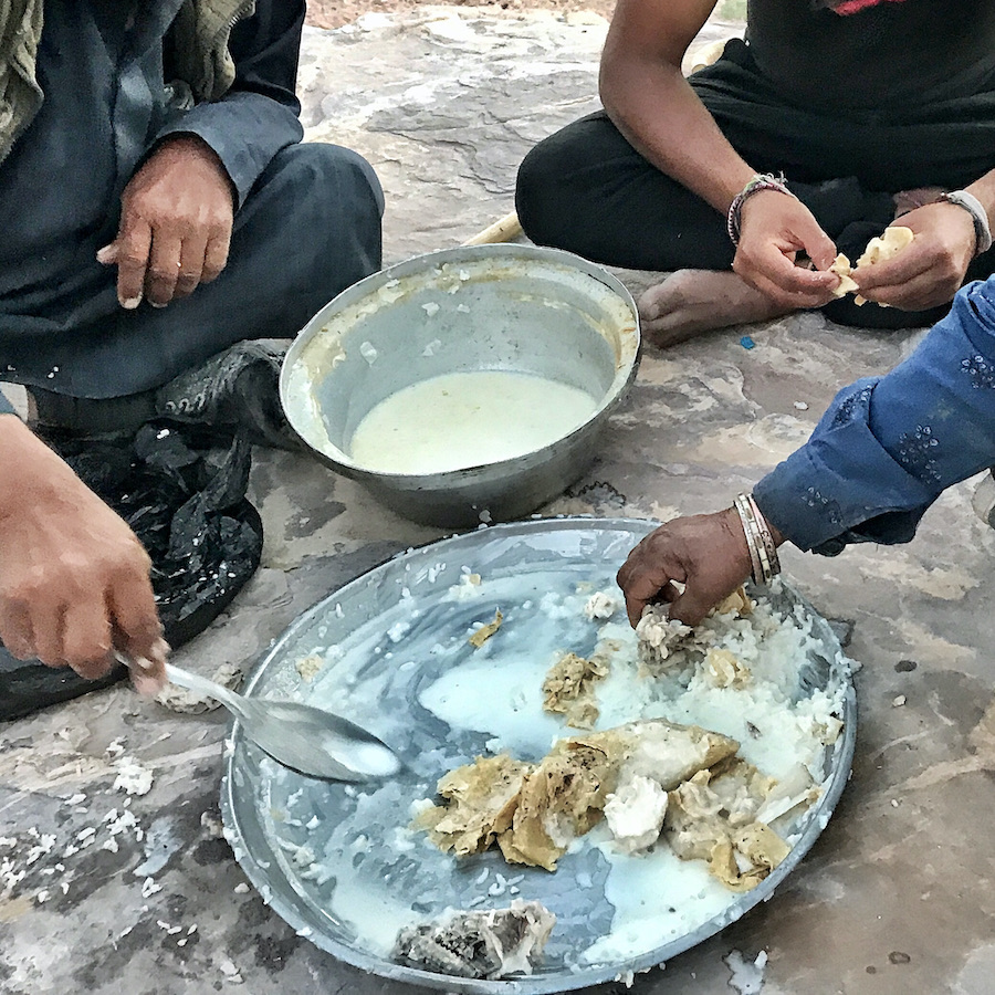 people eating goat off platter on floor