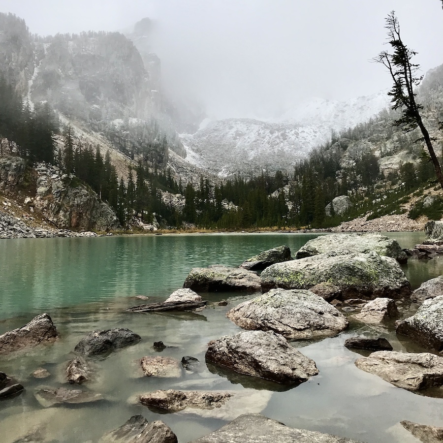 A fog filled basen with a lake with rocks coming into view