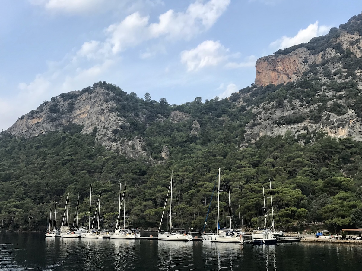 A small marina set near mountains behind a dingy being pulled through the sea