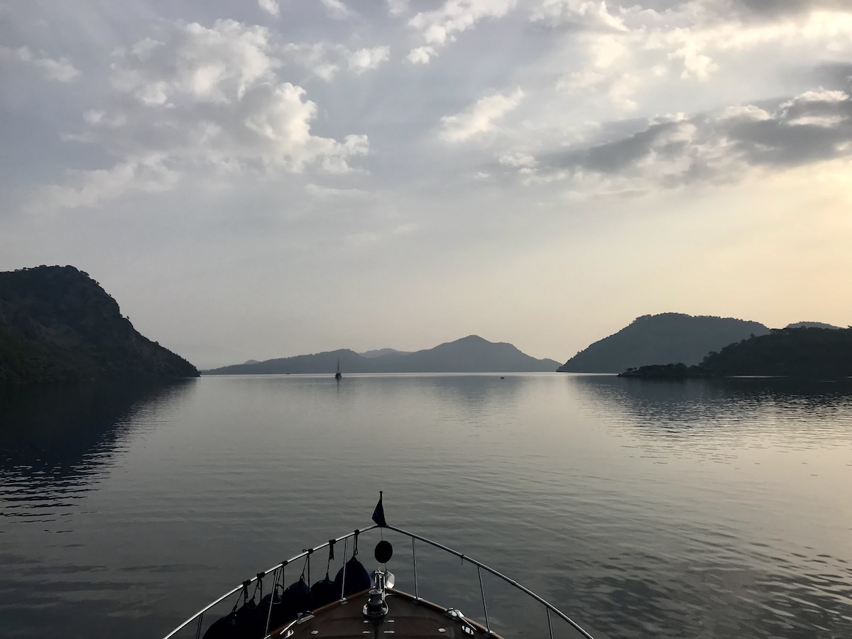 Looking over the bow of a boat heading into reflective waters clouds and moutains in the distance