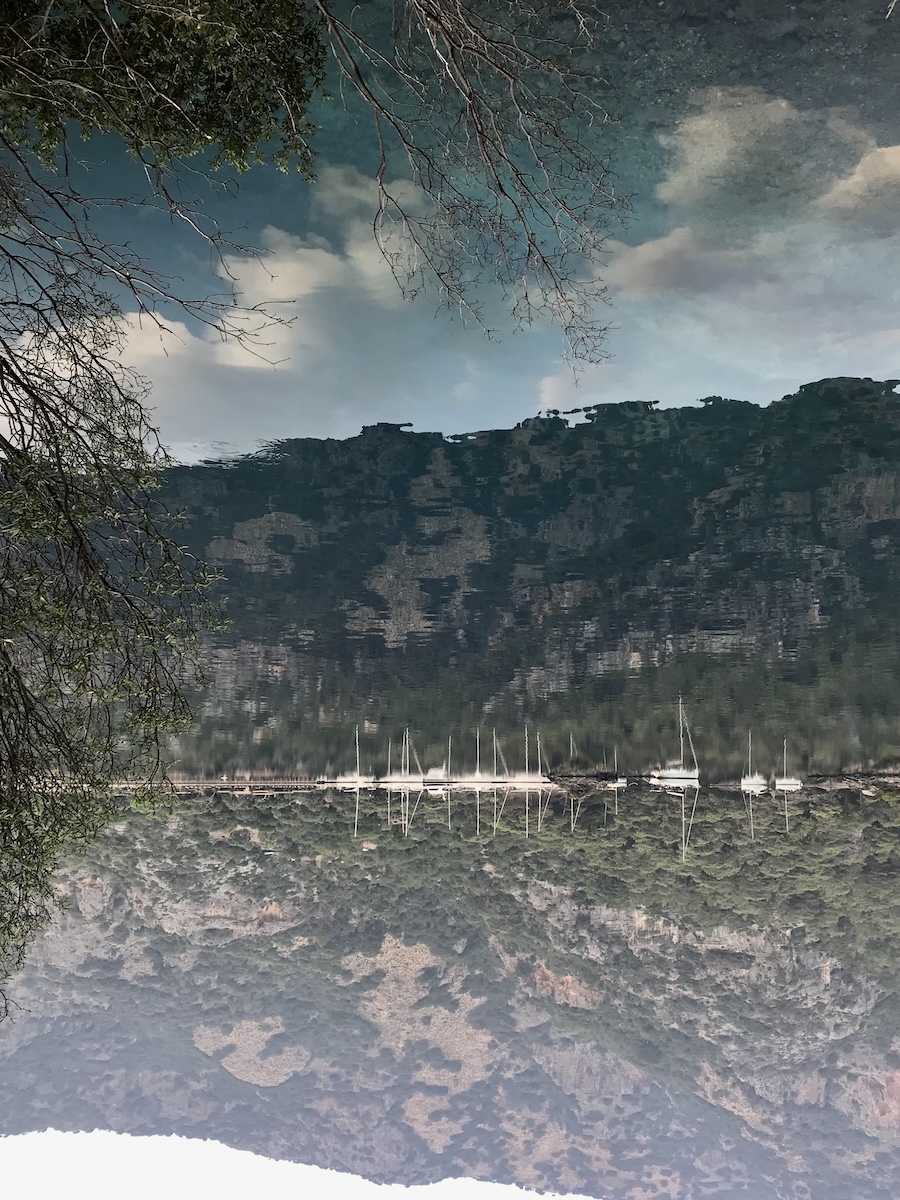 Dreamy image of the reflection of mountains and boats in the sea upside down