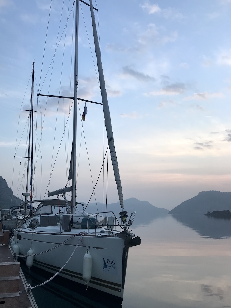 A sailboat docked next to shore at sunrise with orange skies and reflection in the sea