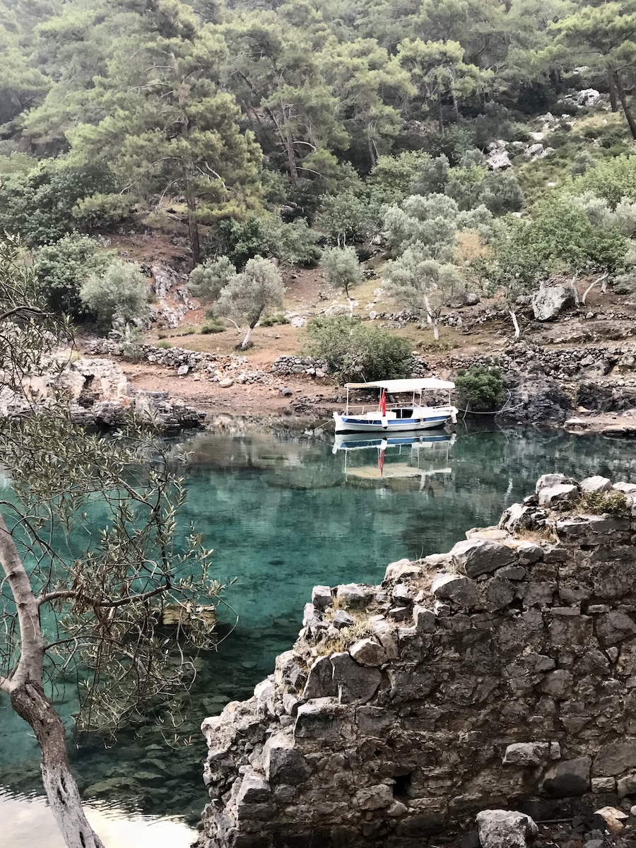 A boat floats in the clear aqua water beyond stone ruins