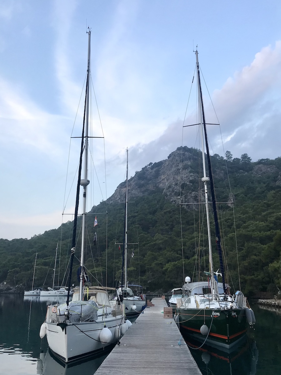 Two sailboats on either side of the wooden walkway with a mountain in the background