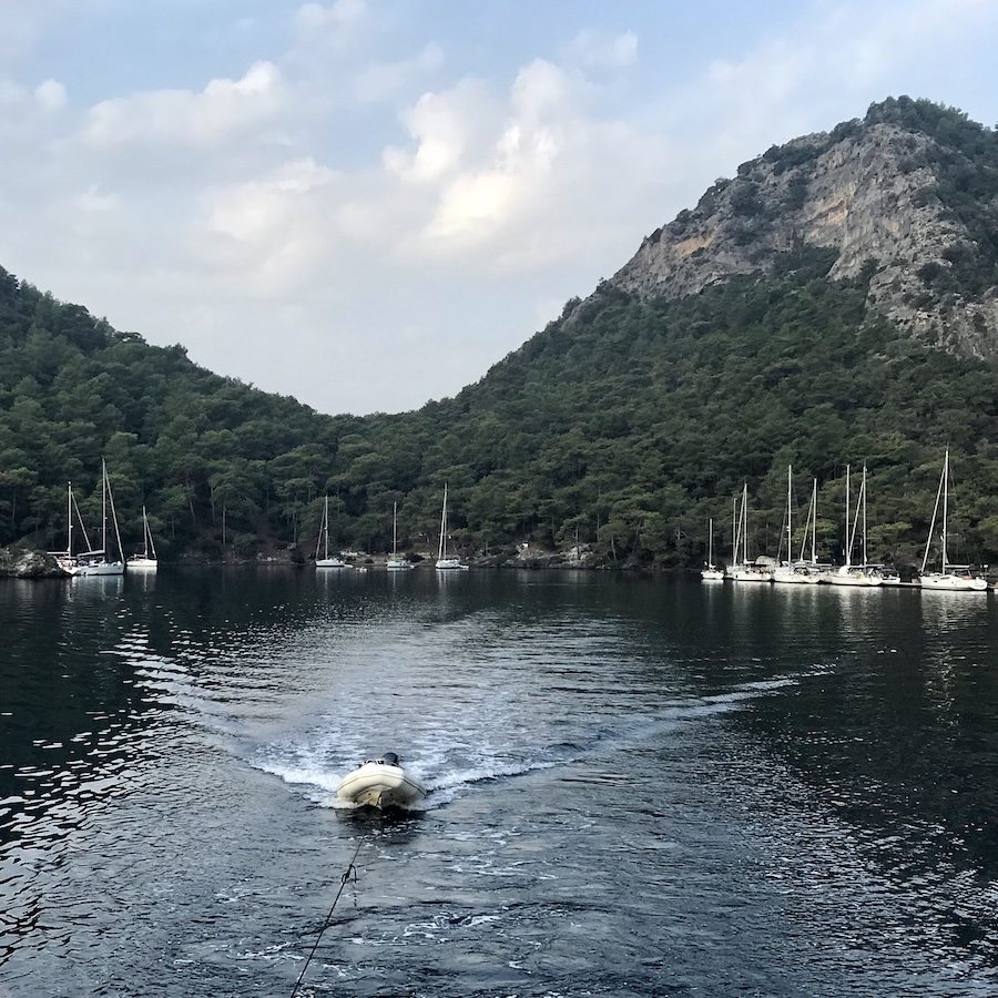 A small marina set near mountains behind a dingy being pulled through the sea