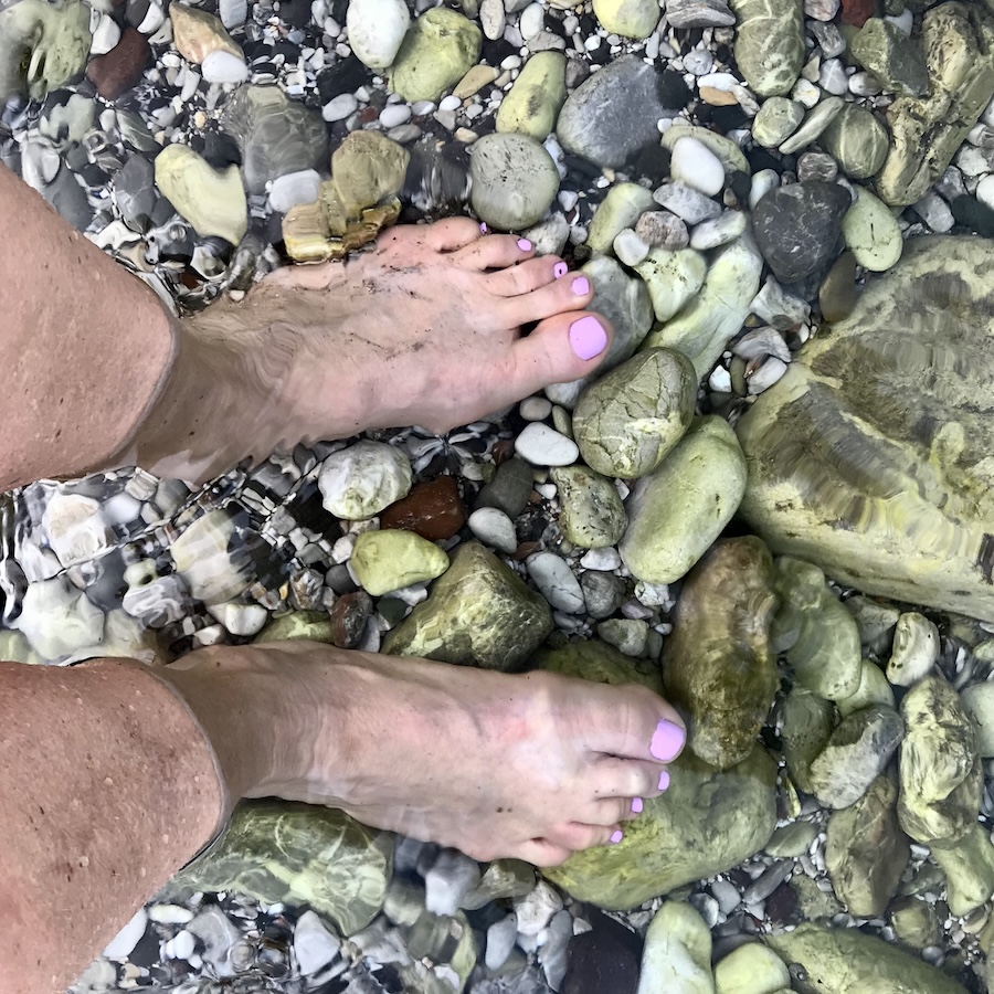 The crystal-clear turquoise waters of the Aegean Sea reveal my toes beneath the surface, perfectly capturing the tranquil beauty of our Blue Voyage.