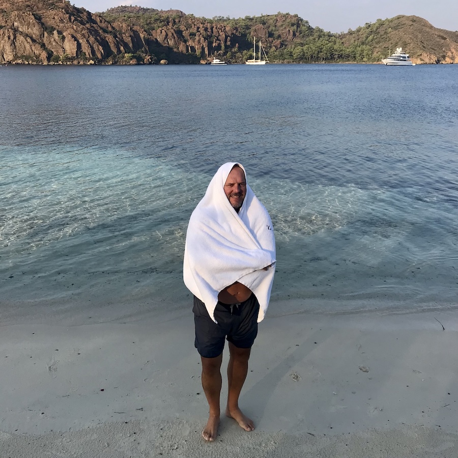 Man with towel on head walking away from ocean