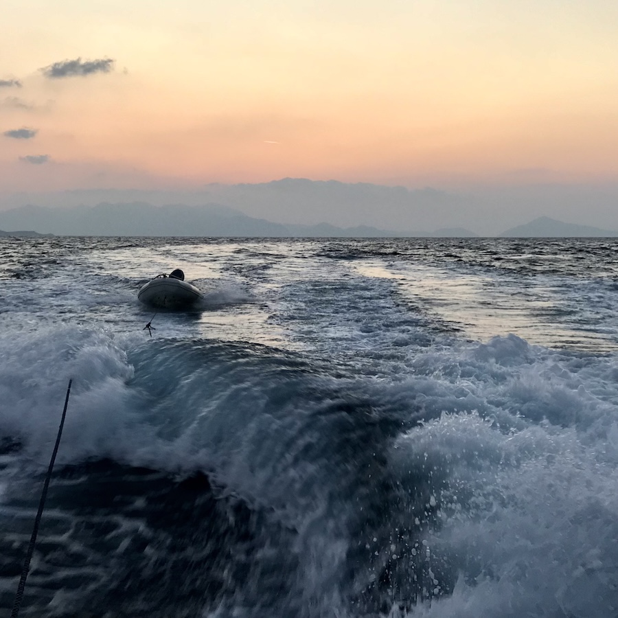 Our dingy floats behind the wake of the boat waves whitewater glowing in the sunset of the Aegean sea