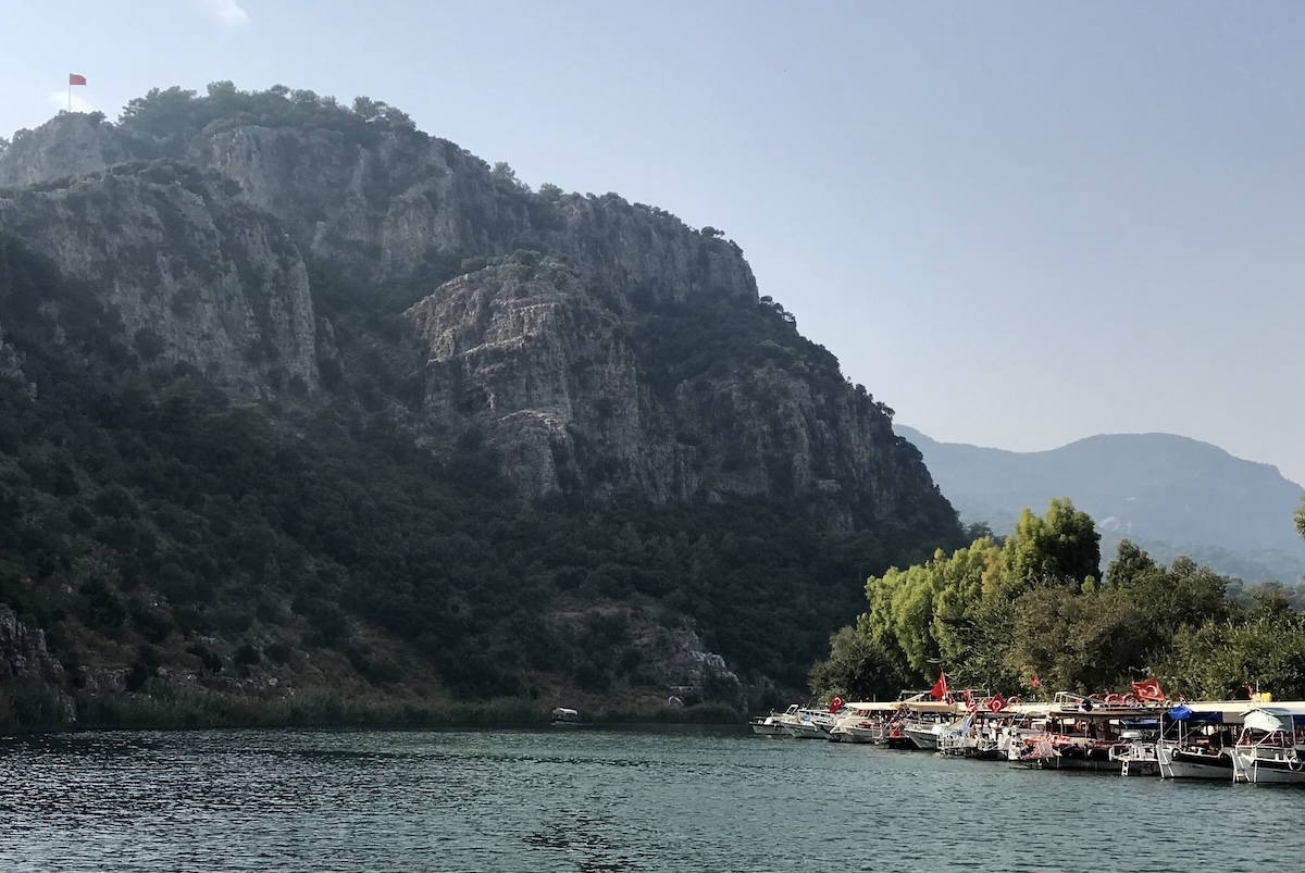 A waterway heads towards sunlite mountain with fisherman's boats docked on the shore on the right