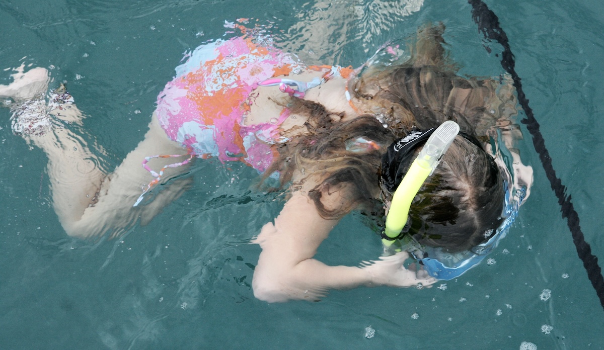 girl floating in ocean water looking down with snorket and mask