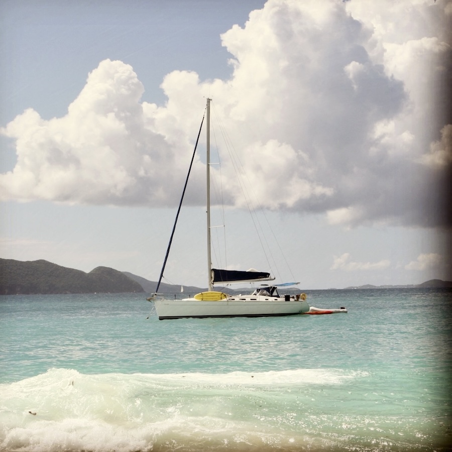 A sailboat on light green ocean with clouds behind
