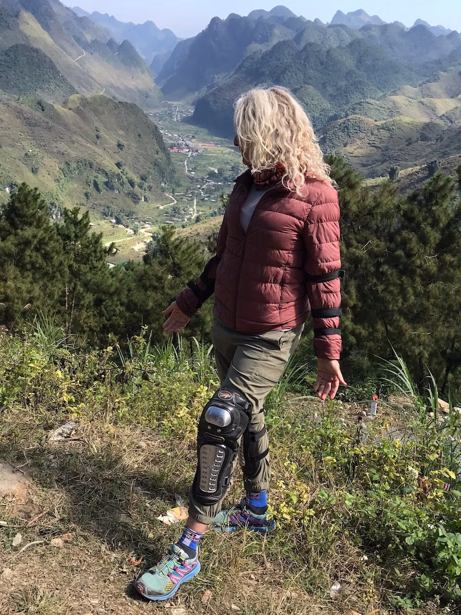 Profile of woman standing with motorcycle pads on her legs in front of mountains in Ha Giang loop, Viet Nam